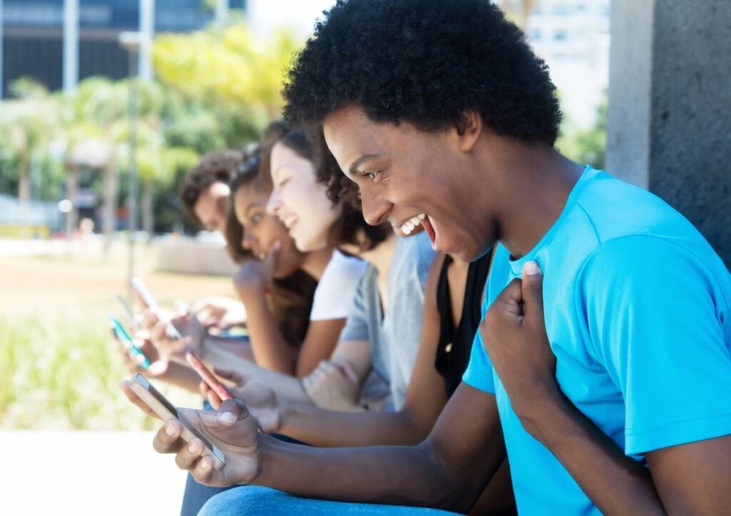 A group of young people happily engaging with their smartphones outdoors.