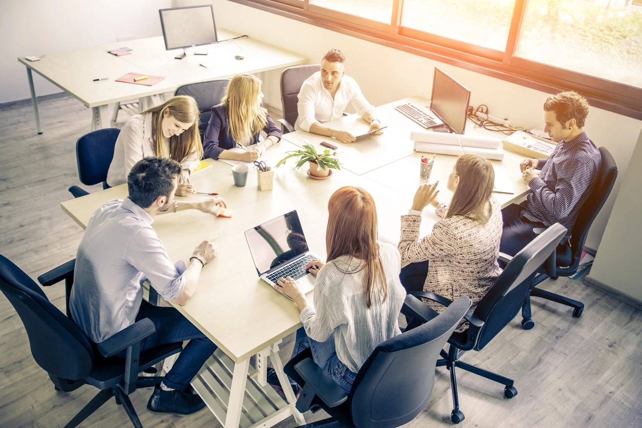 A group of people in a modern office setting engaged in a meeting around a large table.